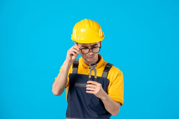 Front view of male worker in yellow uniform looking at pliers on blue 
