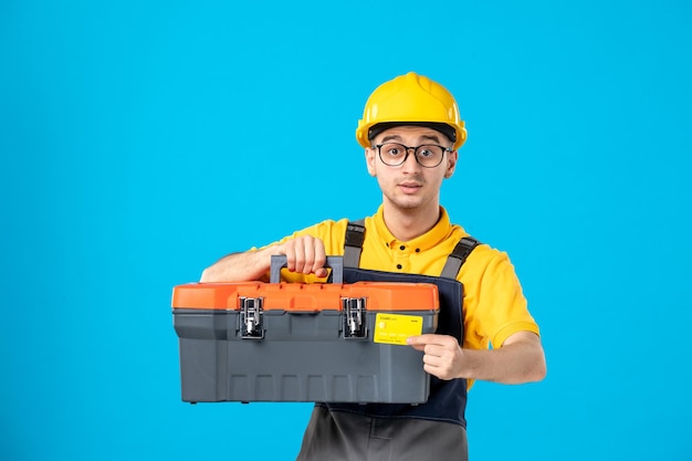 Вид спереди работника-мужчины в желтой форме с банковской картой и ящиком для инструментов на синем