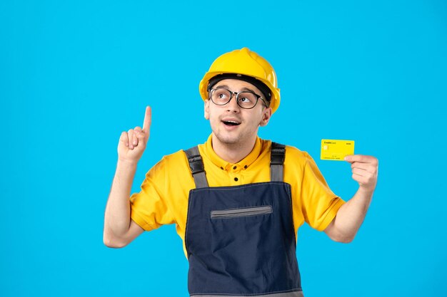 Front view of male worker in yellow uniform with credit card on blue 
