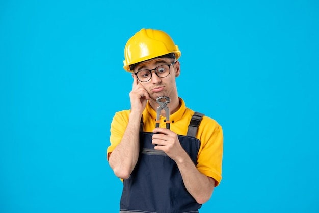 Front view of male worker in yellow uniform with pliers on blue 