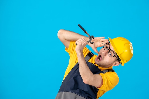 Front view of male worker in yellow uniform with pliers on blue 