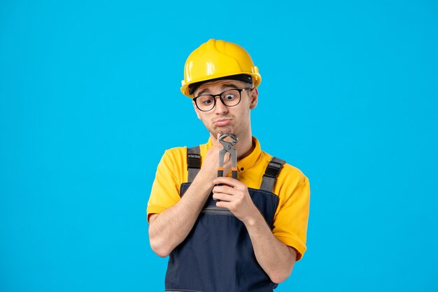 Front view of male worker in yellow uniform with pliers in his hands on blue 