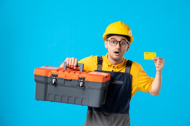 Front view male worker in yellow uniform with tool box and credit card on blue