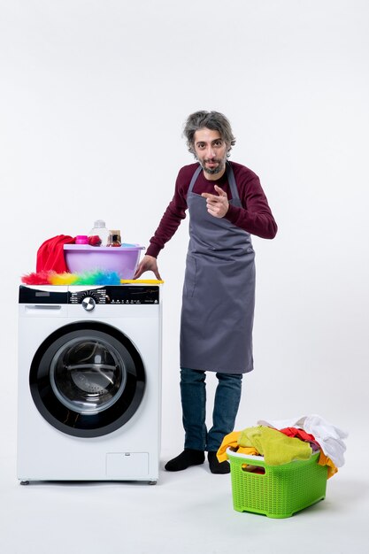 床の白い隔離された壁の洗濯機の洗濯かごに手を置くエプロンの正面図の男