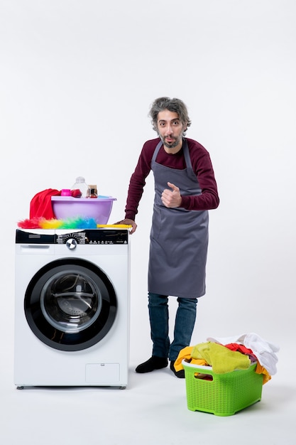 Front view man in apron putting hand on a washer laundry basket on floor white wall