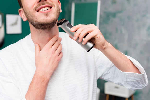 Free photo front view of man in bathrobe using trimmer