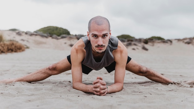 Front view of man on the beach exercising yoga positions on sand