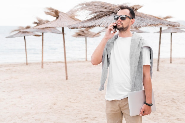 Free photo front view of man on beach holding laptop and talking on smartphone