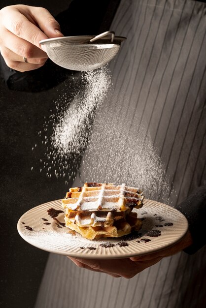 Front view of man coating waffles with powdered sugar