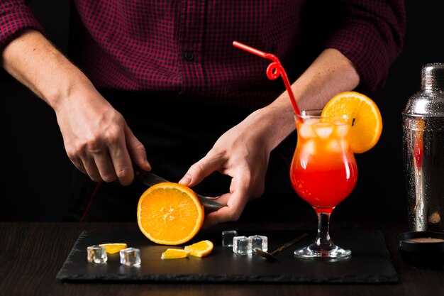 Front view of man cutting orange for cocktail