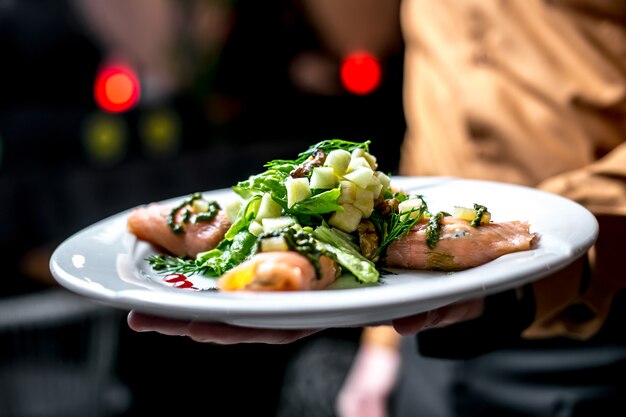 Front view a man holds a plate with vegetable salad with red fish with greens