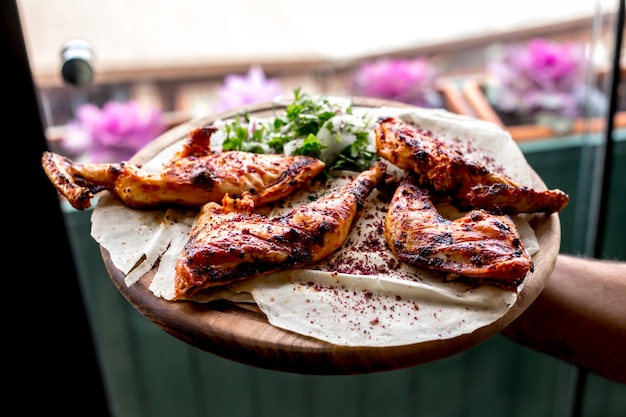 Foto gratuita vista frontale un uomo tiene un vassoio con cosce di pollo alla griglia su una pita con cipolle ed erbe