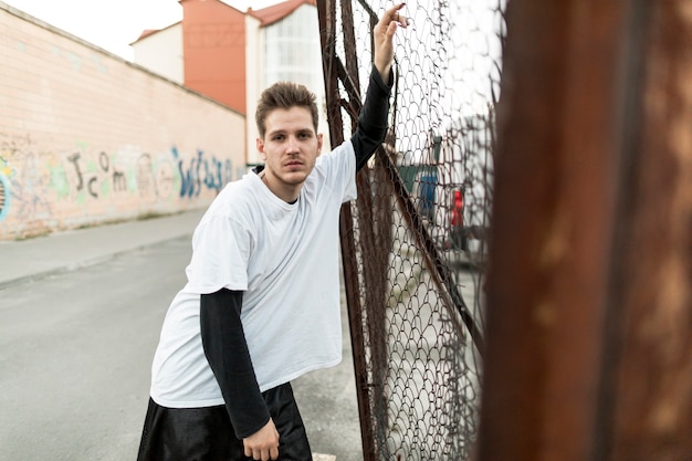 Front view man leaning against a fence