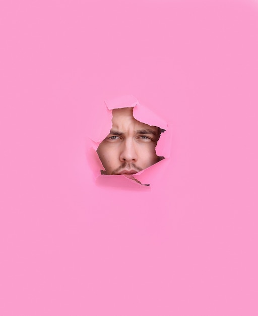 Front view of man looking through a hole in a pink background