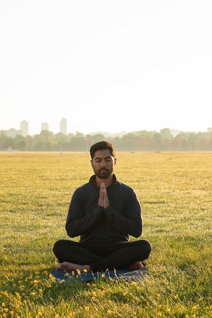 Front view of man meditating outdoors on yoga mat