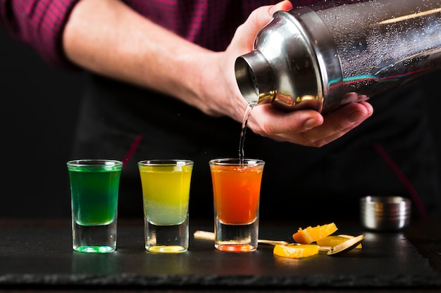 Free photo front view of man pouring cocktail in shot glasses