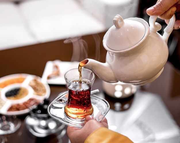 Front view a man pours tea in a glass of armudu from a teapot of tea and holds a glass