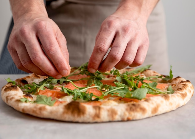 Вид спереди мужчина кладет рукколу на тесто для запеченной пиццы с ломтиками копченого лосося