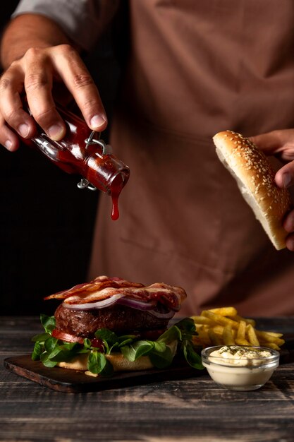 Front view man putting sauce on burger