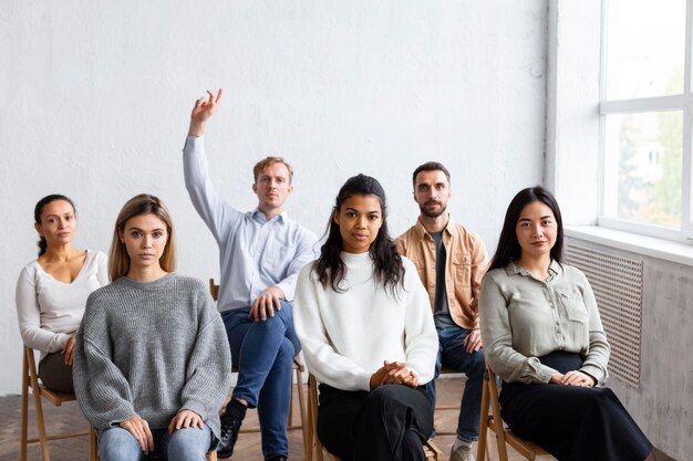 Front view of man raising hand for question at a group therapy session