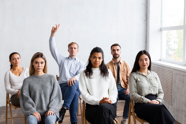 Вид спереди человека, поднимающего руку для вопроса на сеансе групповой терапии