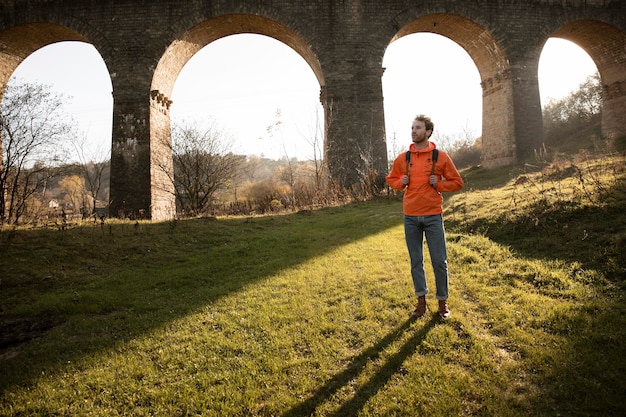 Free photo front view of man on a road trip in nature posing next to aqueduct