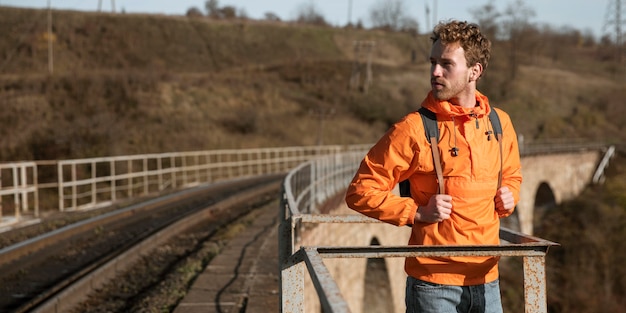 Foto gratuita vista frontale dell'uomo durante un viaggio su strada in posa accanto alla ferrovia