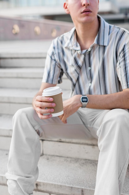 一杯のコーヒーを押しながら屋外の階段に座っている男の正面図