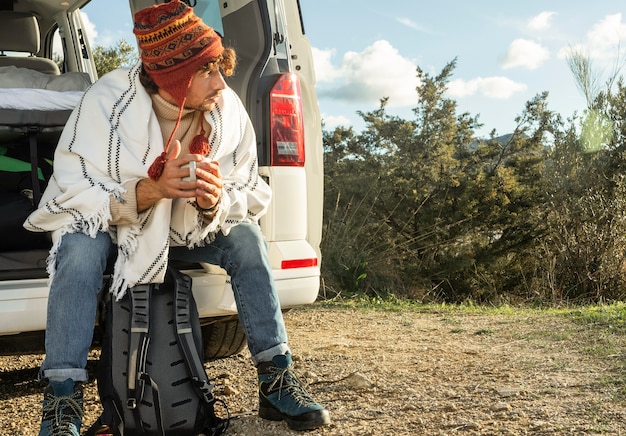 Free photo front view of man sitting on the  trunk of the car while on a road trip