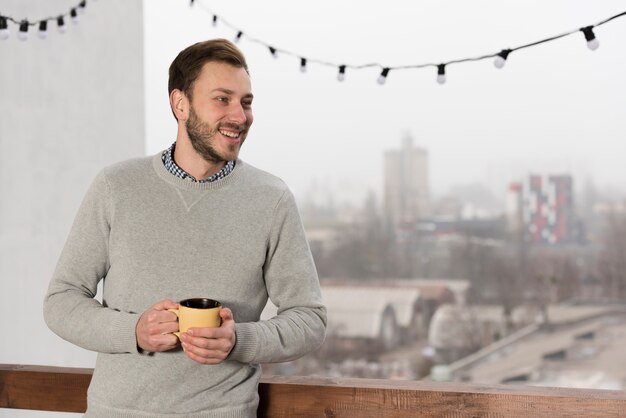 Front view of man in sweater holding cup in hands at home
