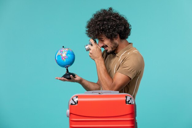 Человек вид спереди в отпуске держит маленький глобус и камеру на синем