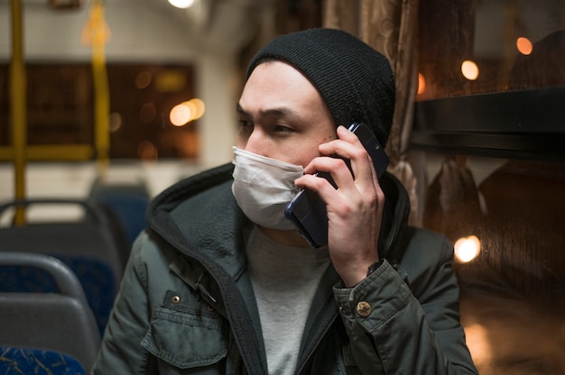 버스에서 의료 마스크를 착용하고 전화로 이야기하는 남자의 전면보기