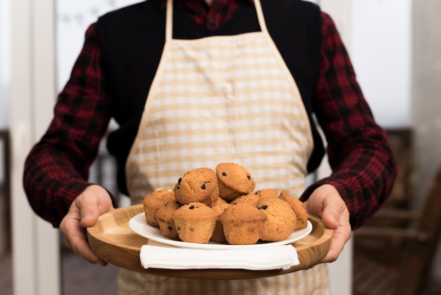 Front view of man with apron holding plate of muffins