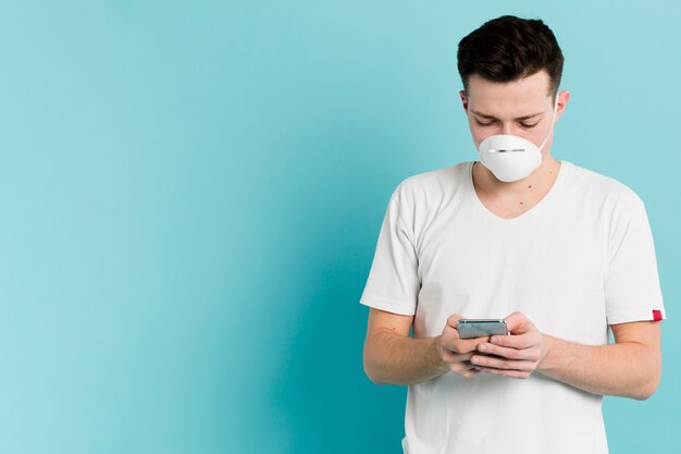 Front view of man with medical mask looking up coronavirus on smartphone