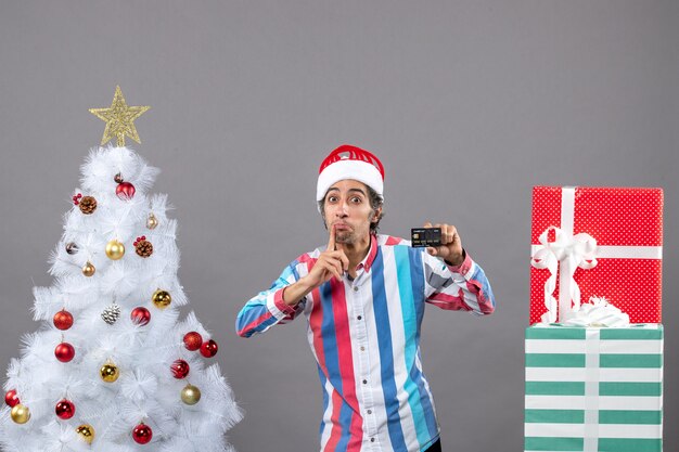 Front view man with prying eyes with card standing near white xmas tree