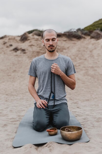 Front view of man with singing bowl and rosary outdoors