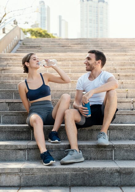 Front view of man and woman drinking water outdoors while exercising