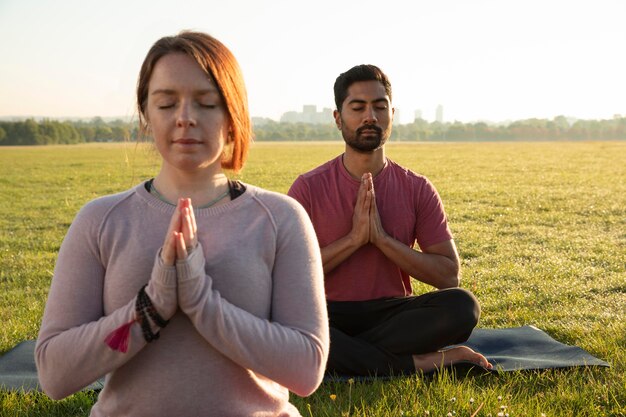 Front view of man and woman meditating outdoors on yoga mats