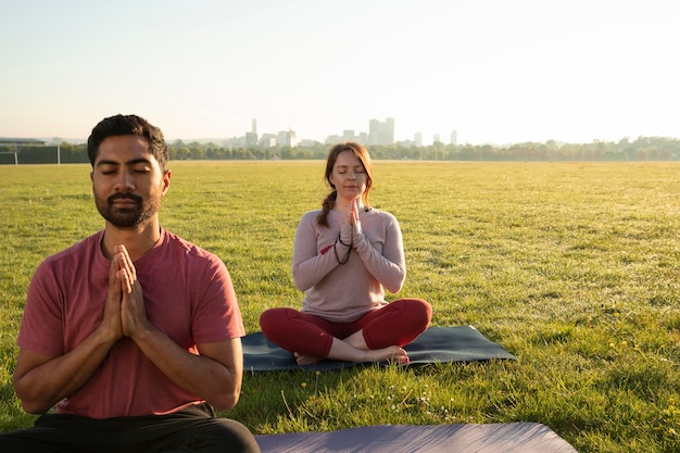 Front view of man and woman meditating outdoors on yoga mats