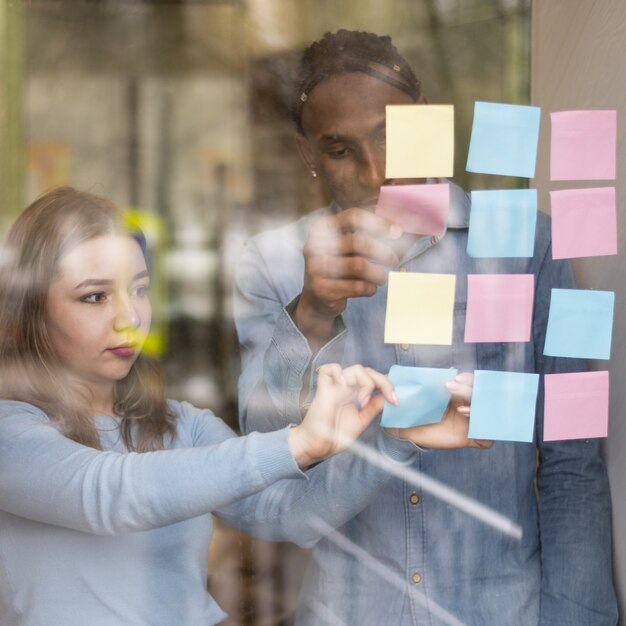 Front view of man and woman putting sticky notes on office window