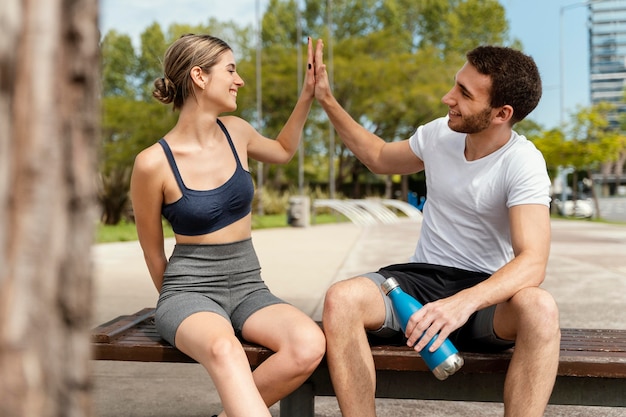 Мужчина и женщина отдыхают на открытом воздухе после тренировки и дают друг другу пять, вид спереди