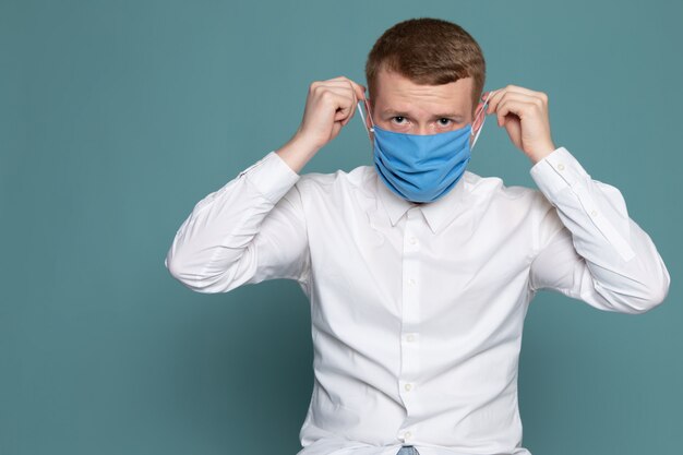 A front view man young wearing blue mask in white shirt on the blue desk