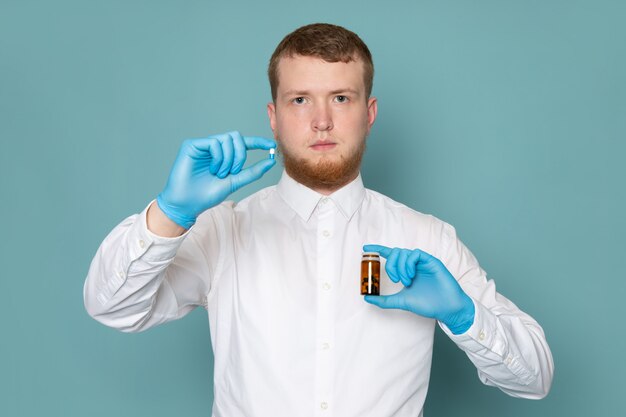 A front view man young in white t-shirt holding pills on the blue floor