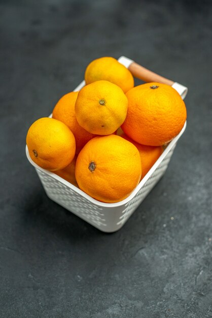 Вид спереди мандарины и апельсины в пластиковой корзине на темном свободном пространстве