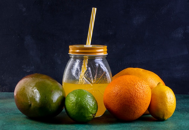 Front view mango with lemon lime orange and juice in a jar with a yellow straw