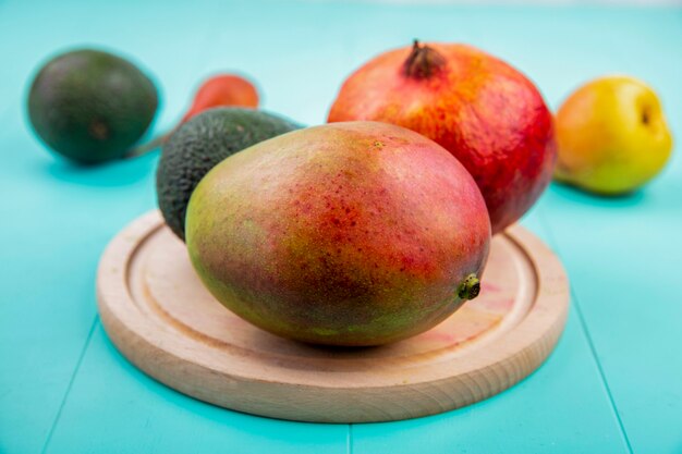 Front view of mango with pomegranate on a wooden kitchen board on blue surface