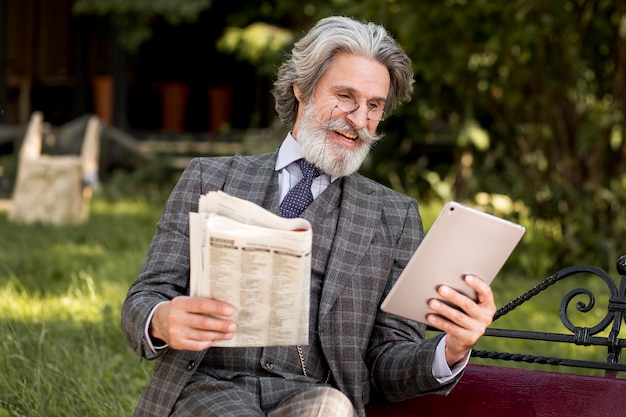 Front view mature male holding newspaper and tablet