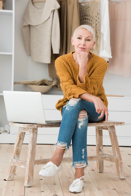 Front view of mature woman posing with laptop on chair