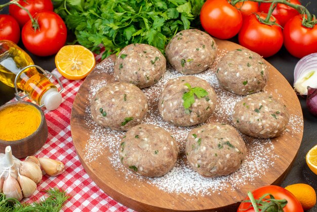 Front view of meat balls on a brown board and rice flour fresh green lemon fallen oil bottle fresh vegetables yellow ginger on red stripped towel on black background