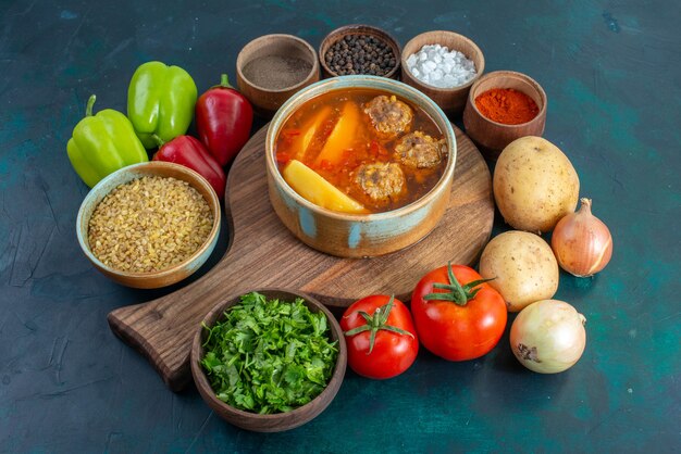スライスしたジャガイモが入った正面図のミートボールスープと紺色の壁に新鮮な野菜が入ったフードスープ肉料理ディナー野菜